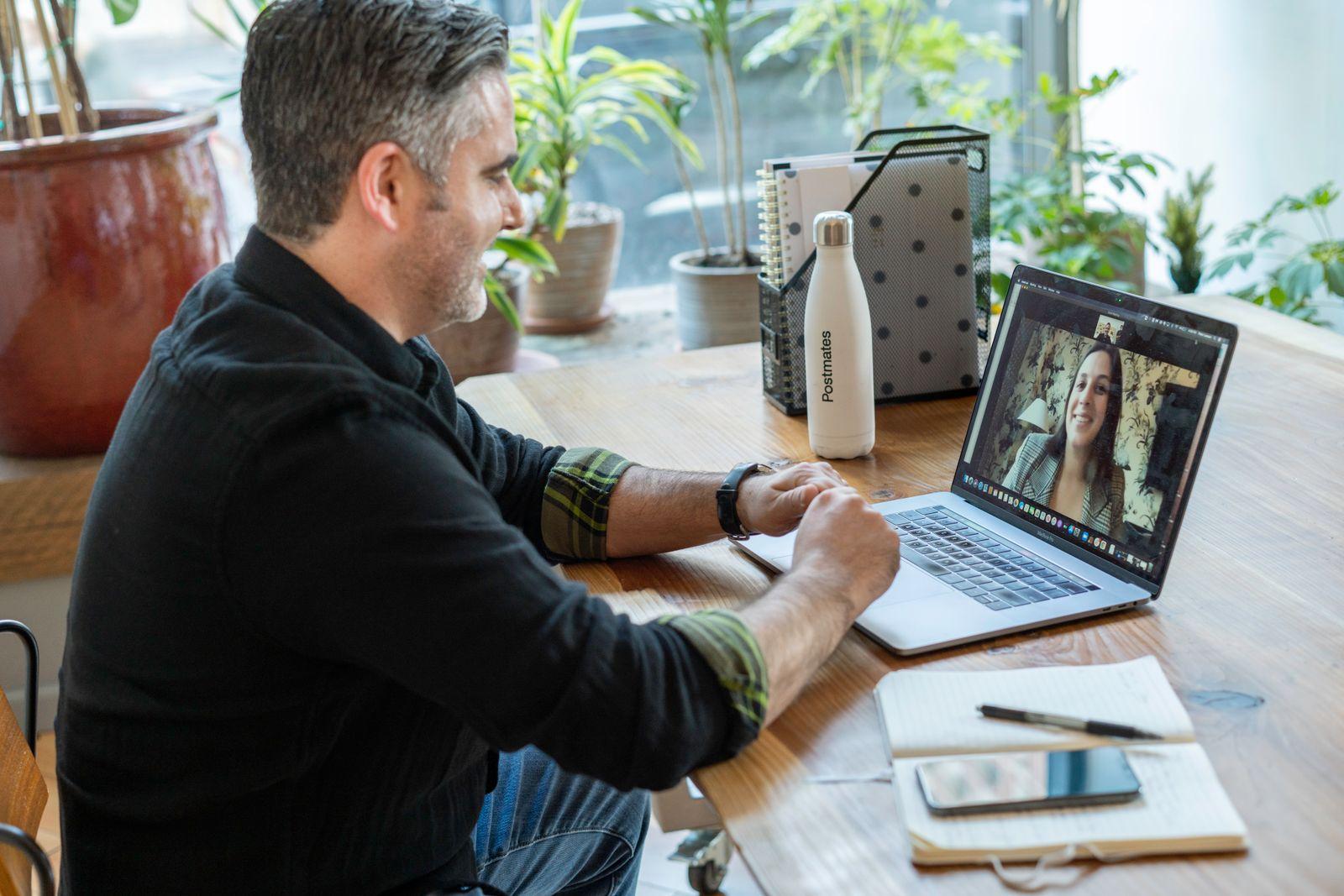 Man smiling at a video call on his laptop at a wooden desk