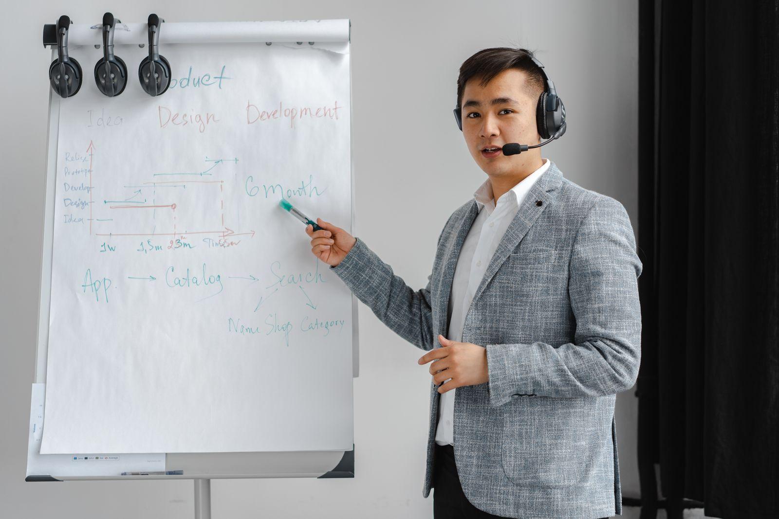 Presenter wearing a headset microphone pointing at a flip chart