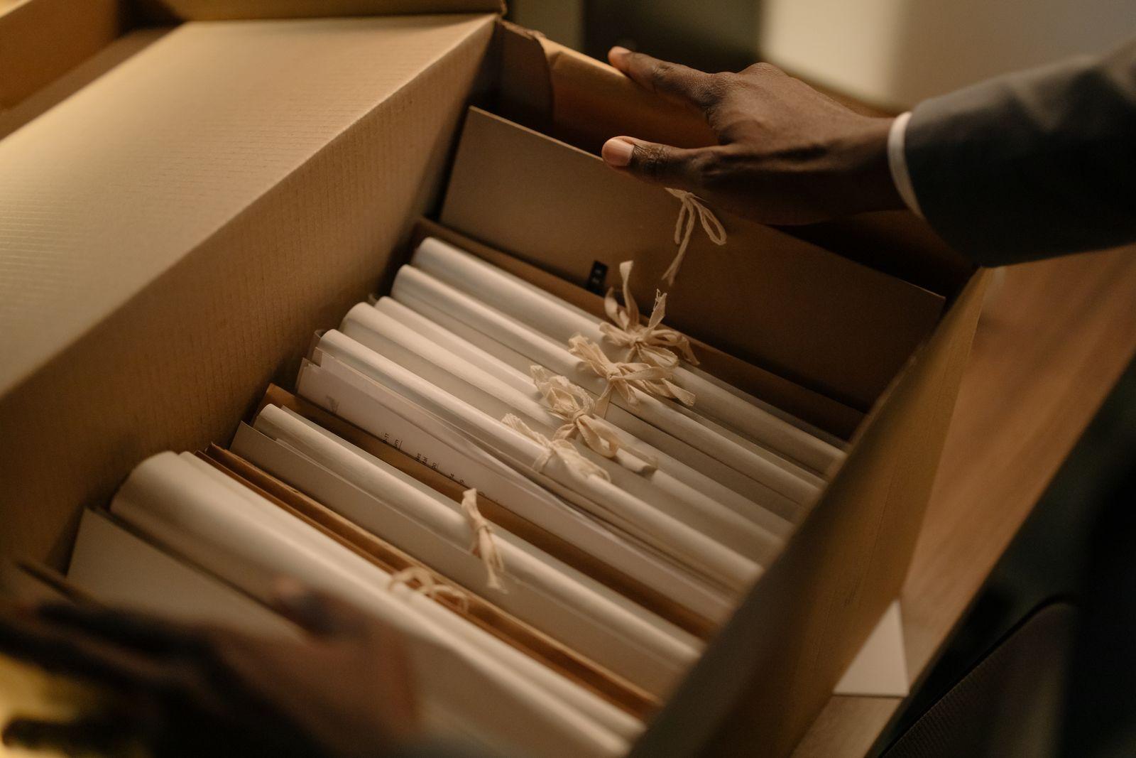 Hands lifting rolled papers tied with string out of an archive box