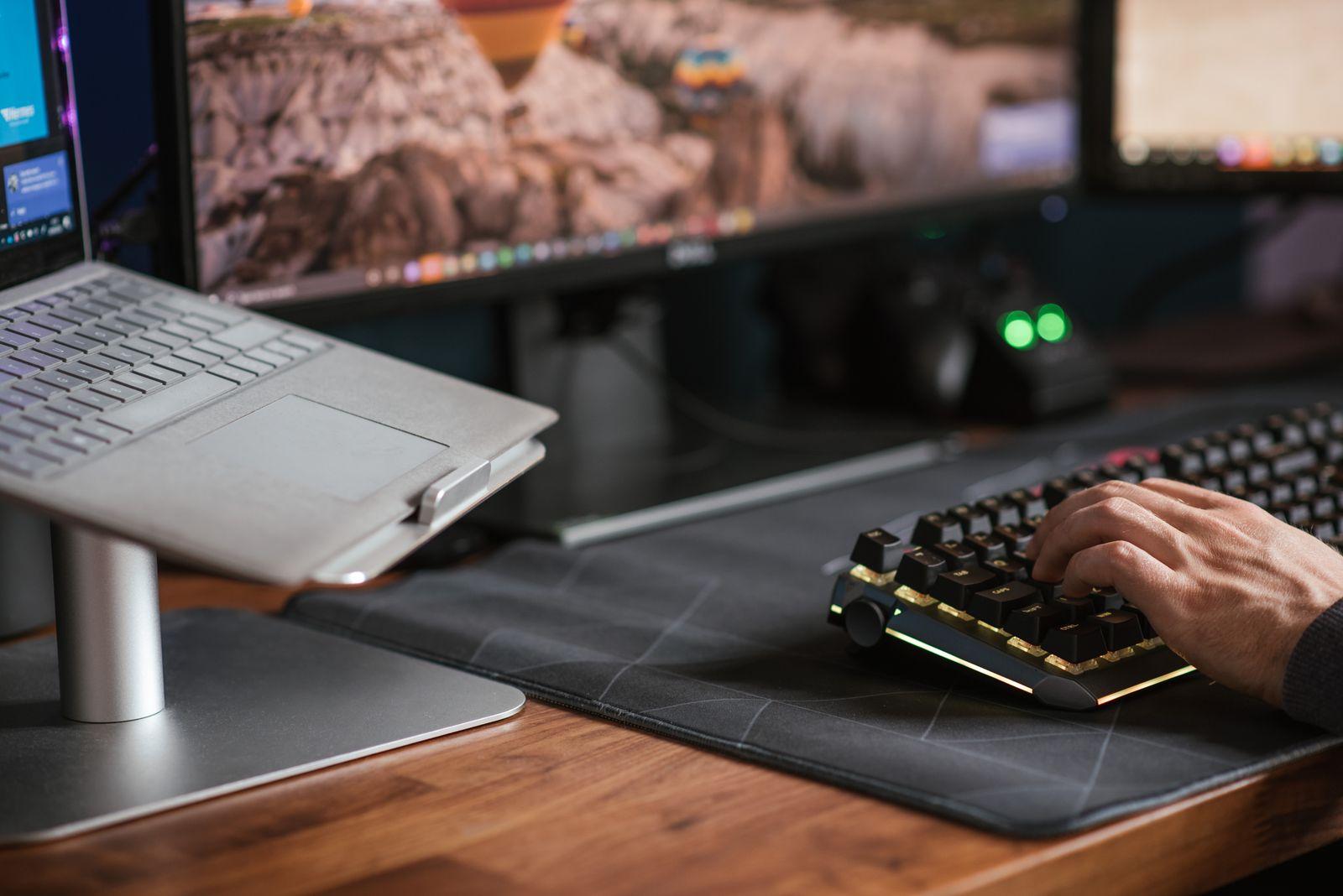 Hand typing on a keyboard next to a laptop on a stand