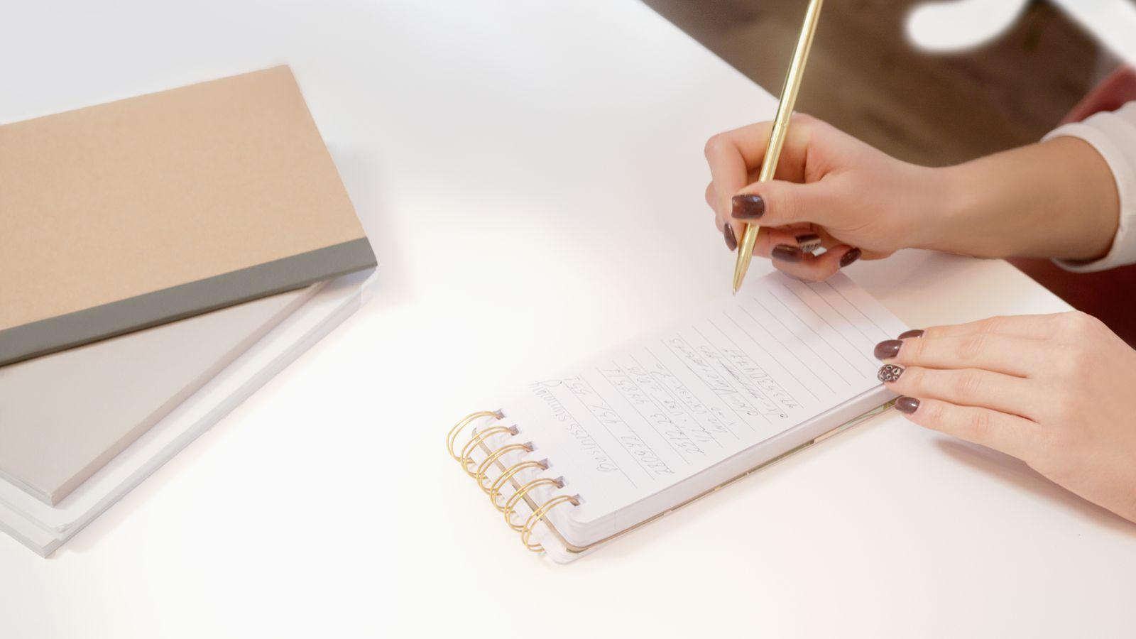 Hand writing in a small spiral notepad with a gold pen