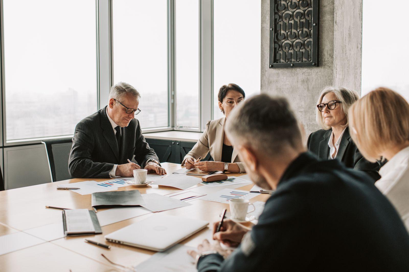 Five colleagues around a boardroom table taking notes on printed reports