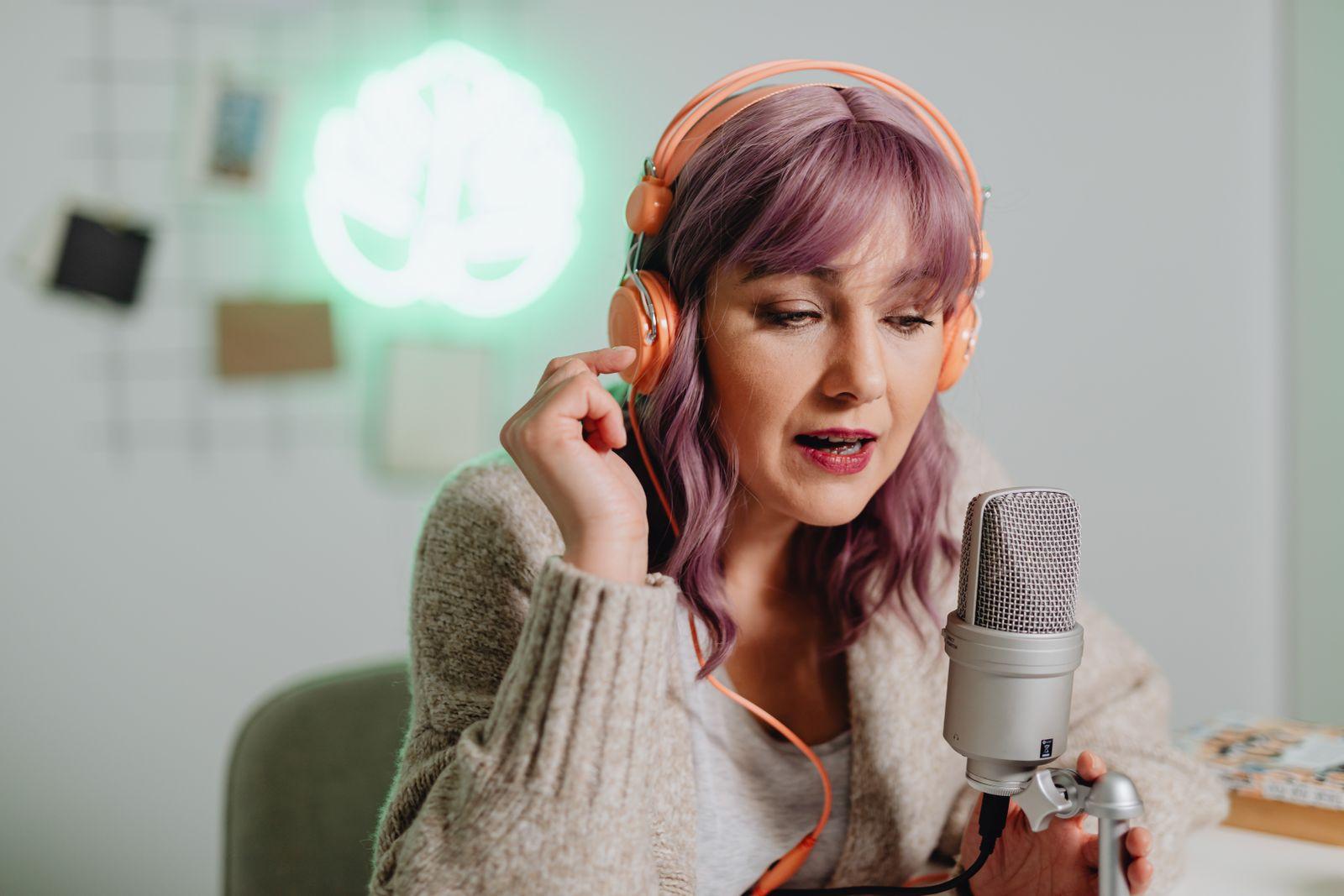 Podcaster in orange headphones speaking into a studio microphone
