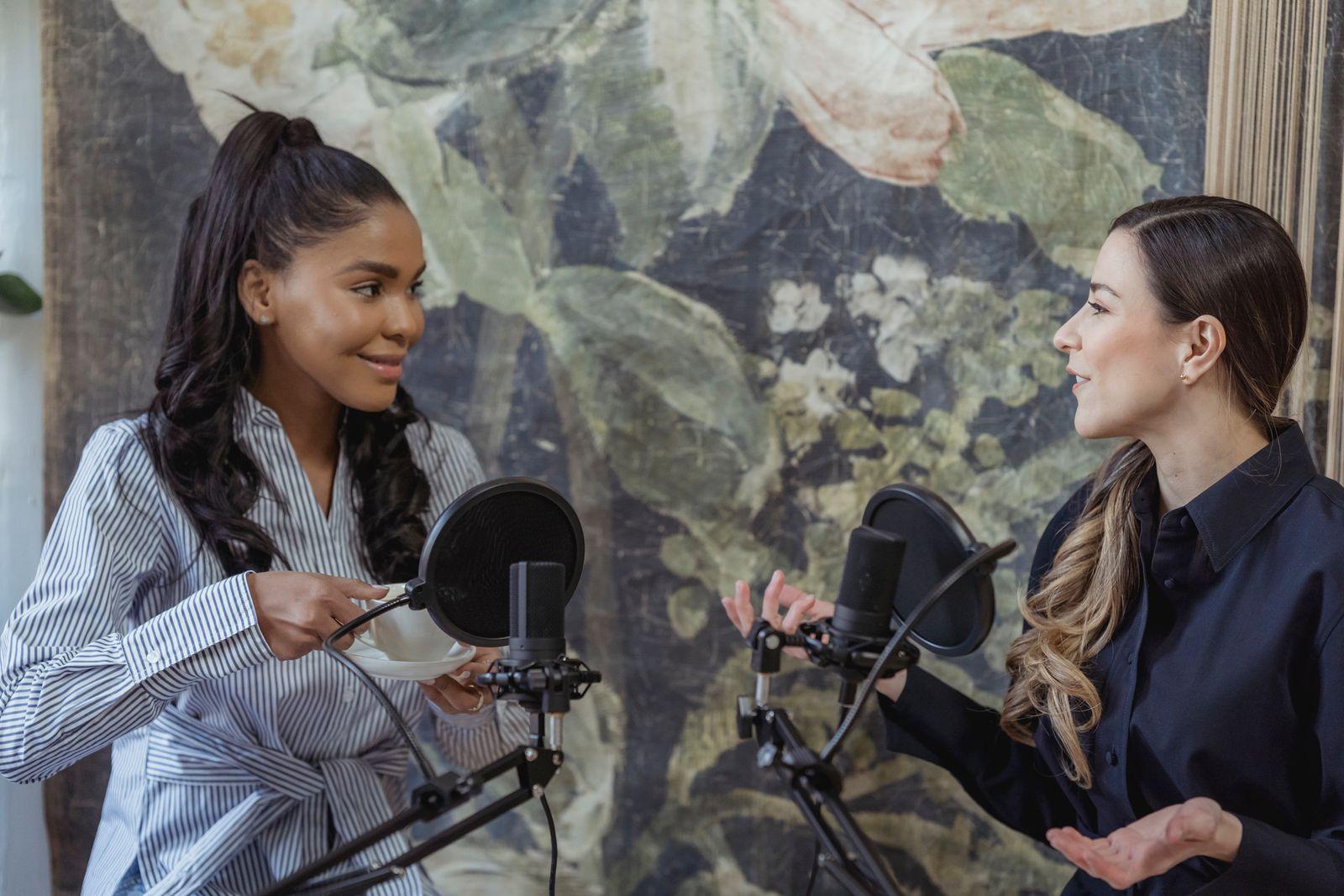 Two podcast hosts talking at microphones with pop filters