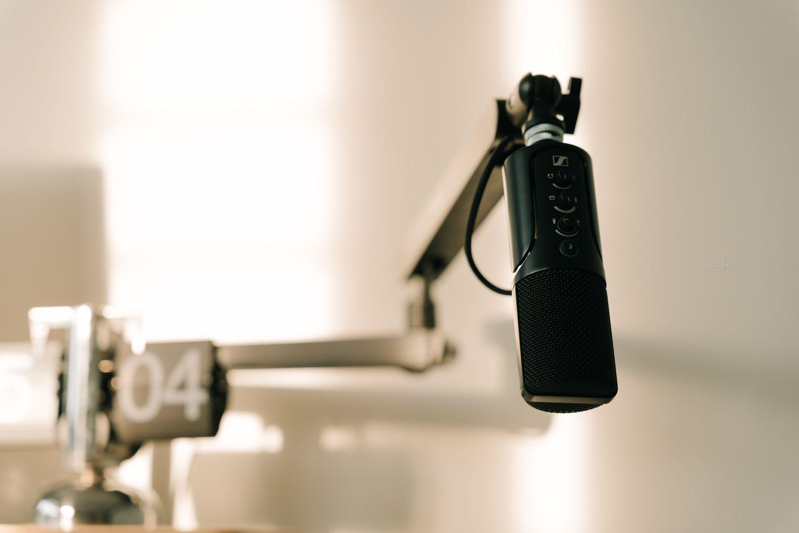 Black podcast microphone on a boom arm in front of a flip clock