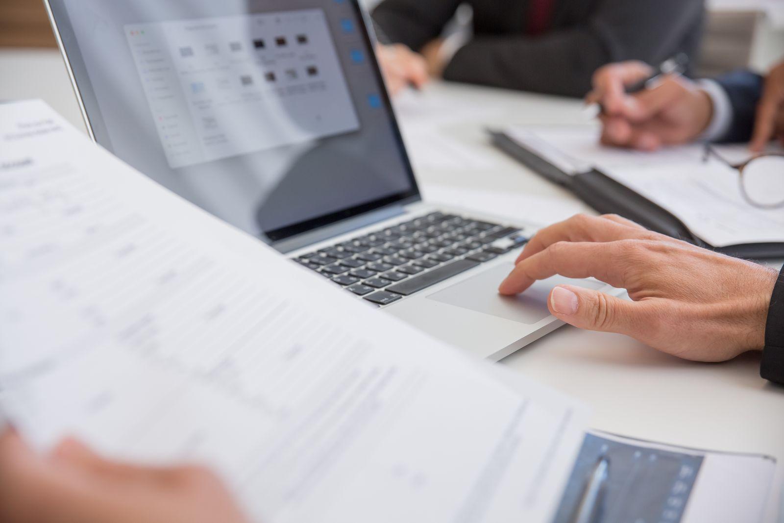 Hands on a laptop next to printed documents on a desk