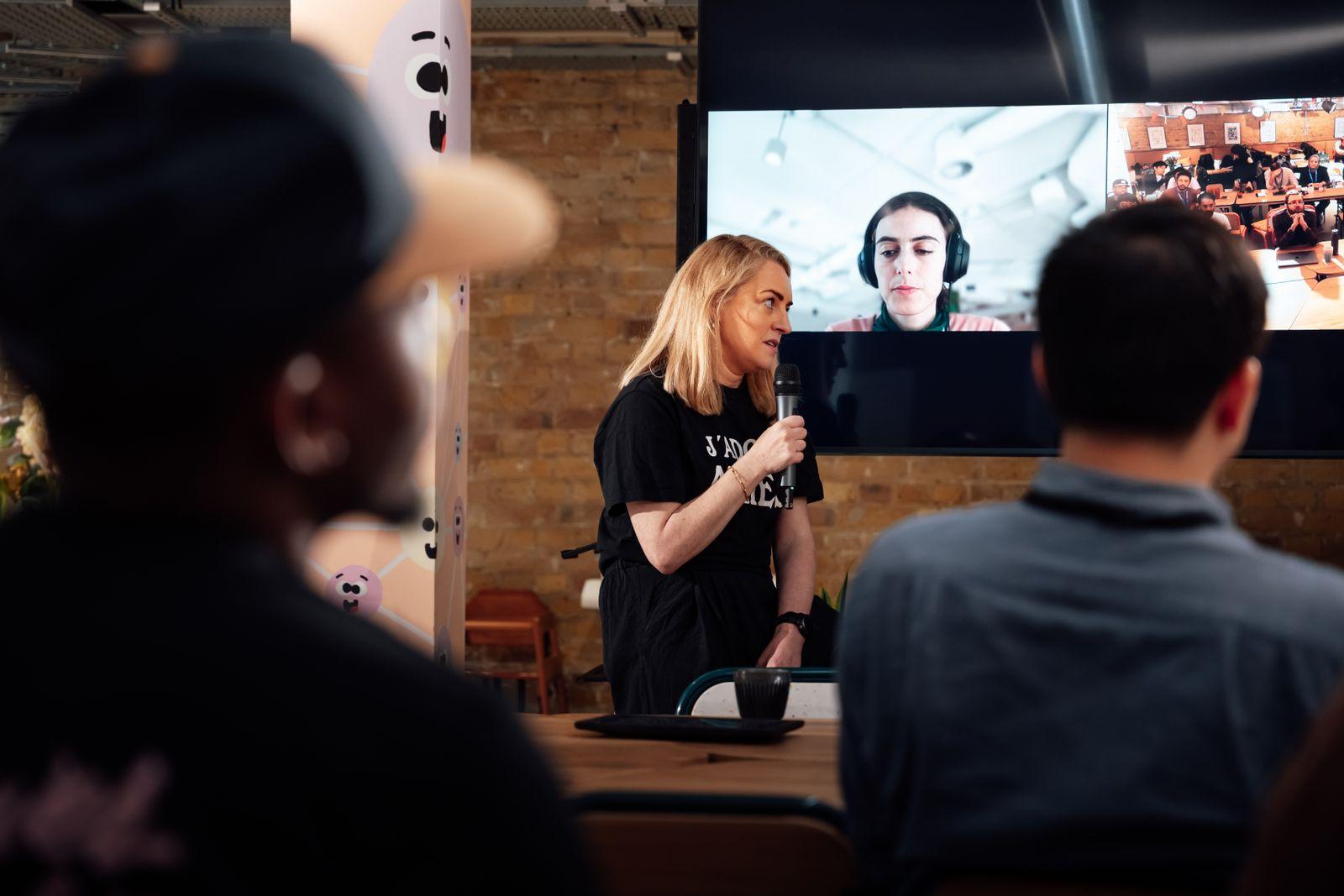 Presenter speaking to a room while a remote participant appears on a large screen
