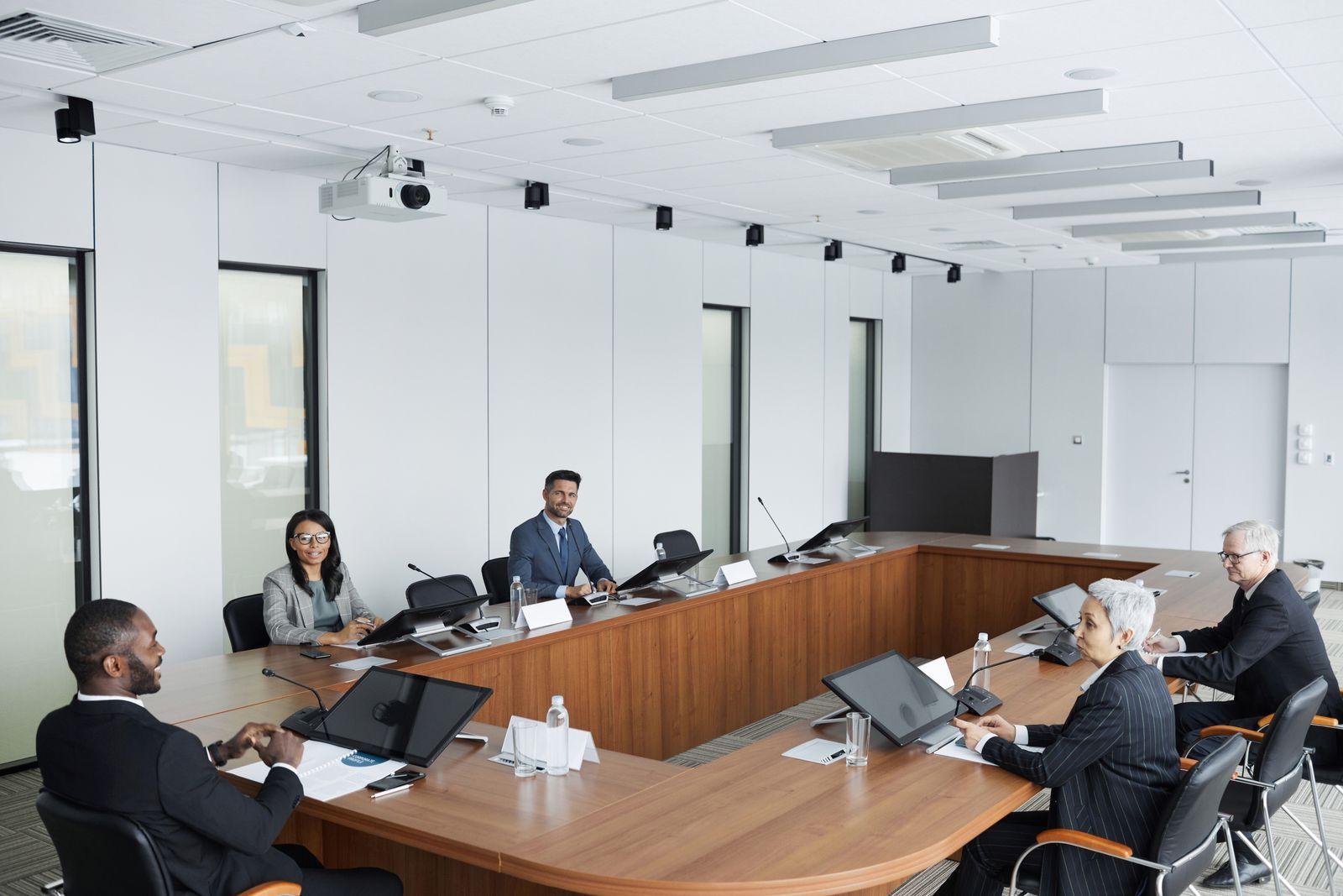 Board members seated around a large conference table with microphones and laptops