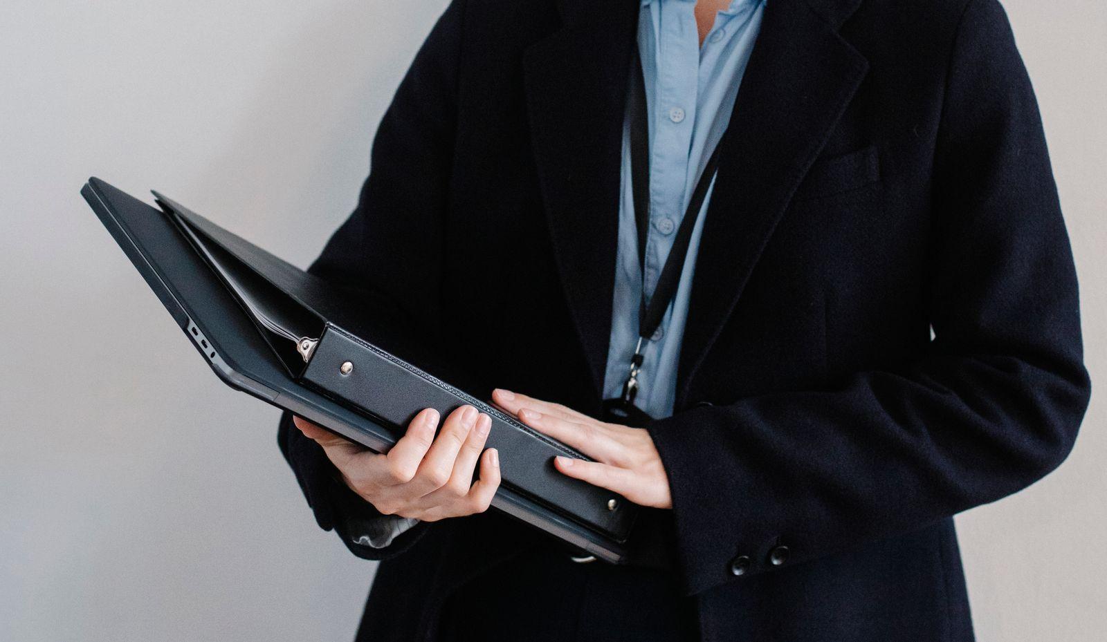 Person in a dark suit holding a black portfolio folder