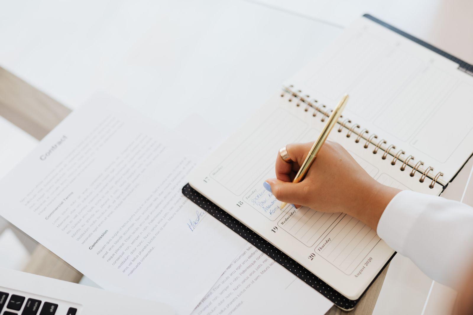 Hand writing in a planner next to a printed document