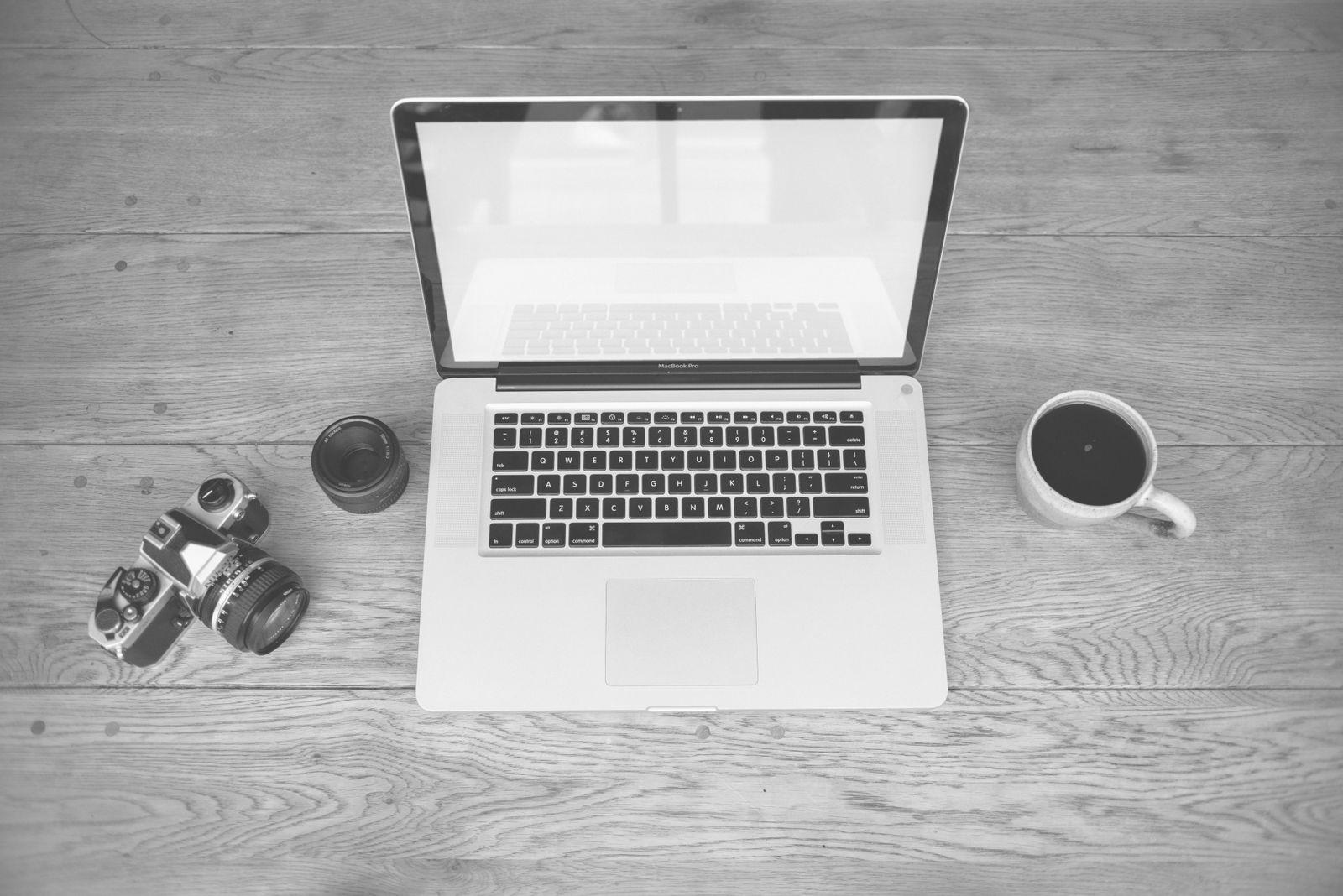 Black-and-white photo of a laptop next to a camera and a cup of coffee