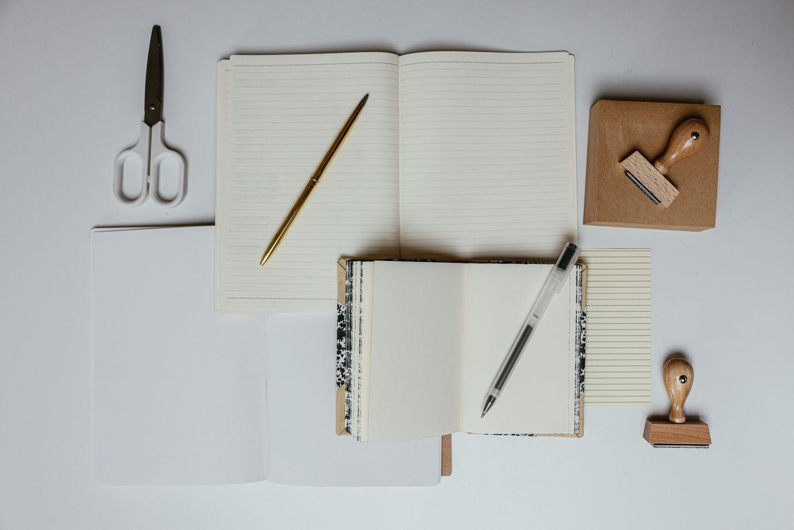 Two open blank notebooks with pens, scissors and rubber stamps on a white desk