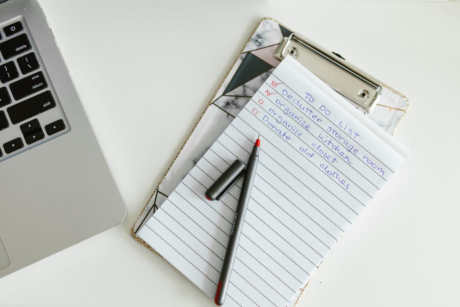 Handwritten to-do list on a clipboard next to a laptop