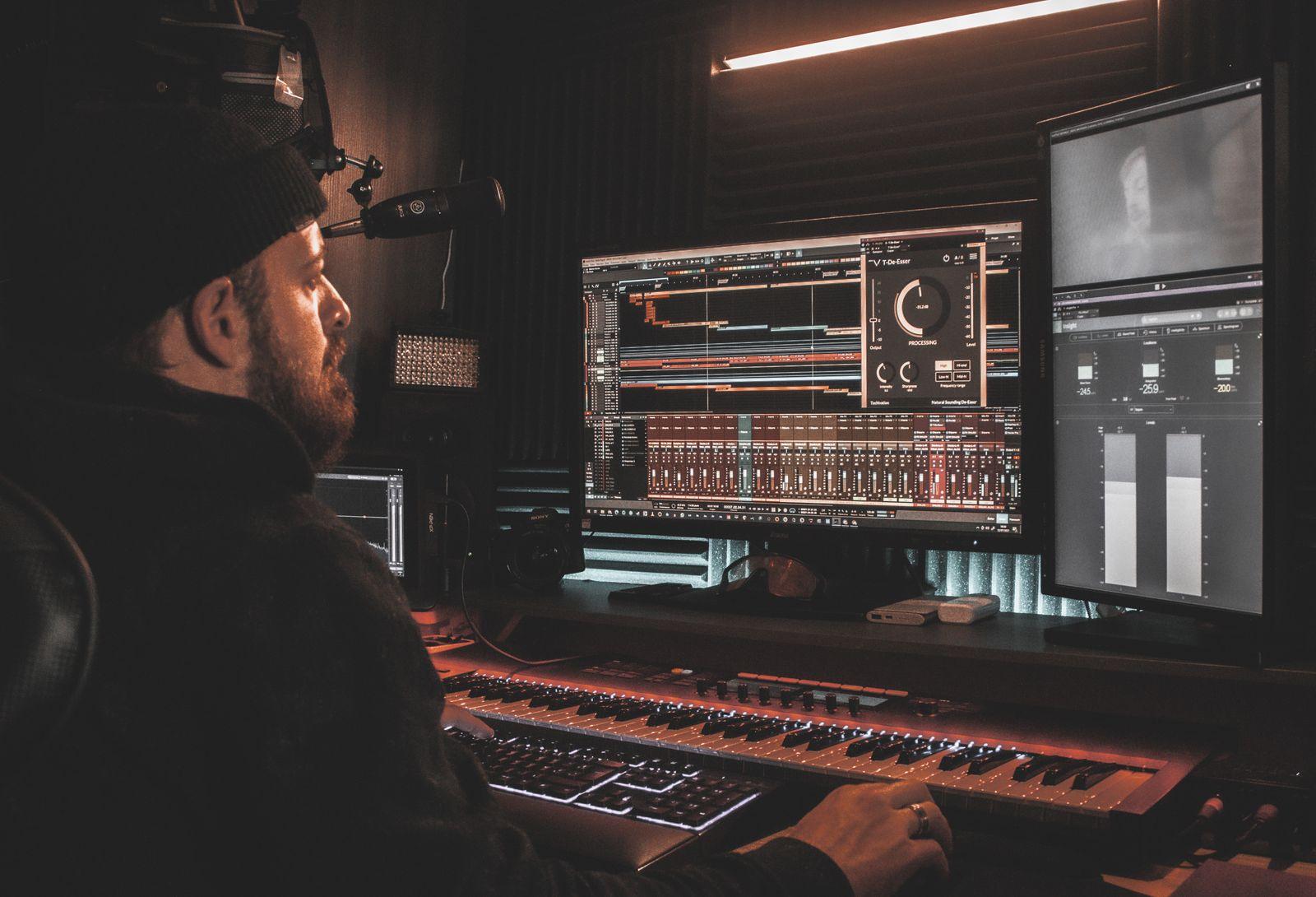 Producer at a studio desk editing audio on two monitors