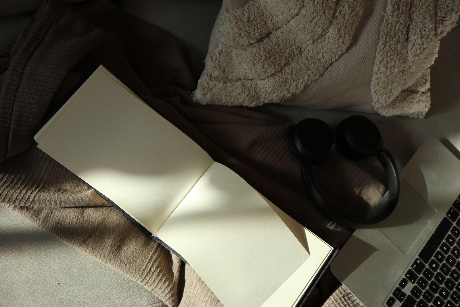 Open blank notebook next to headphones and a laptop