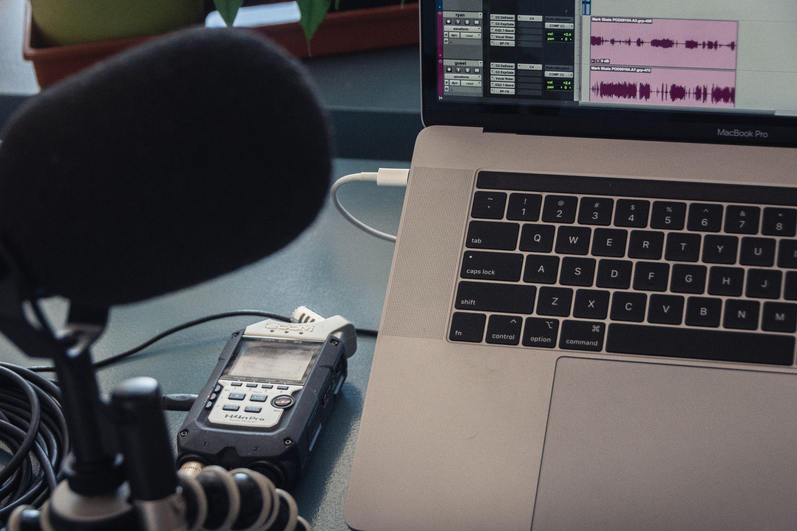 Microphone and handheld audio recorder beside a laptop showing audio waveforms