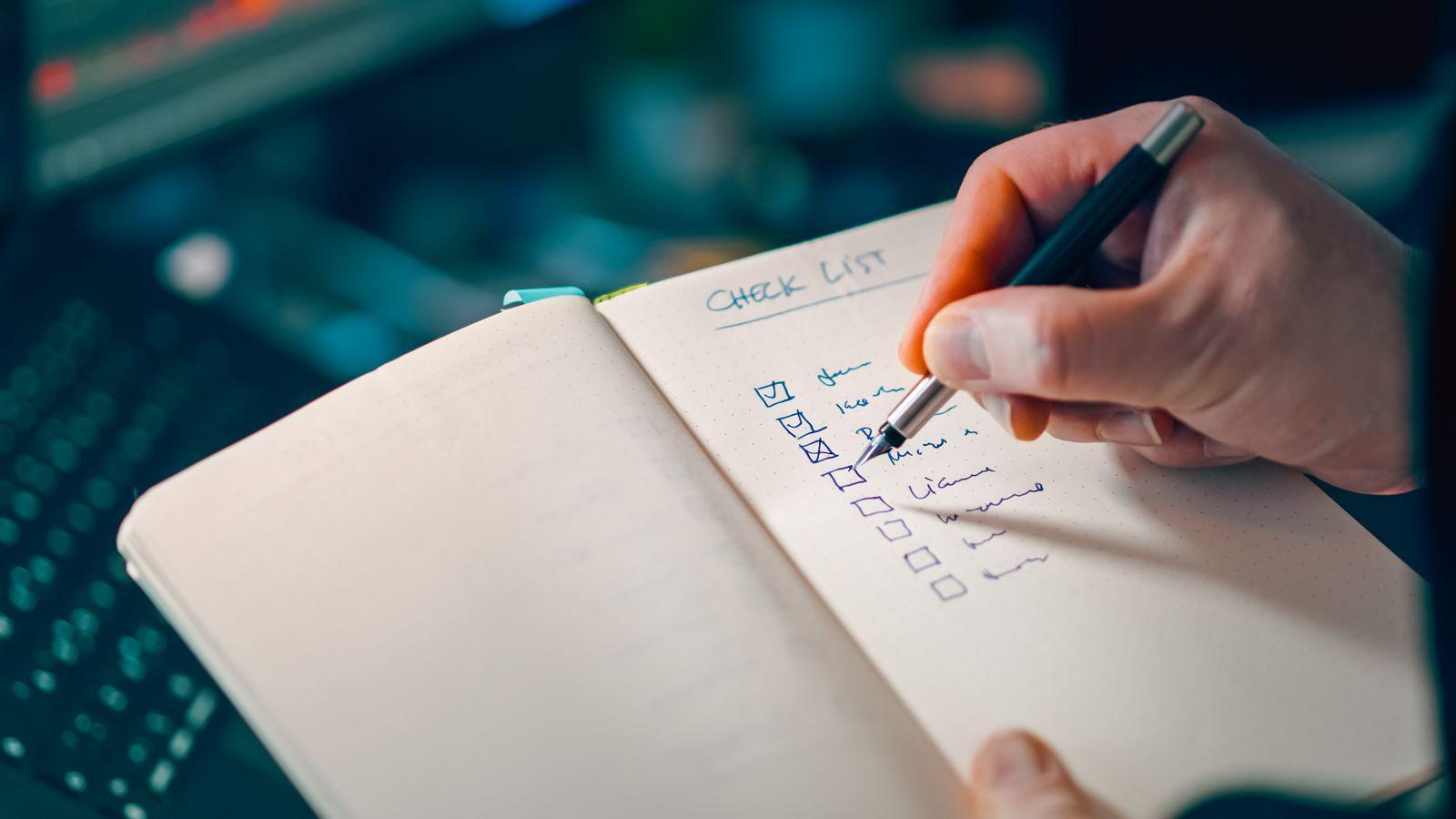Hand ticking items on a handwritten checklist in a notebook