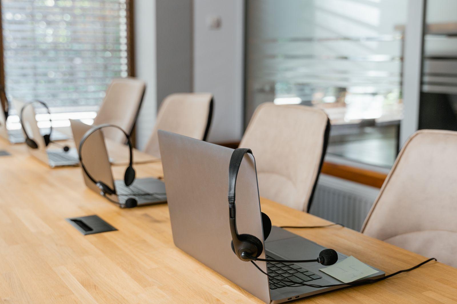Row of laptops and headsets on a long office desk