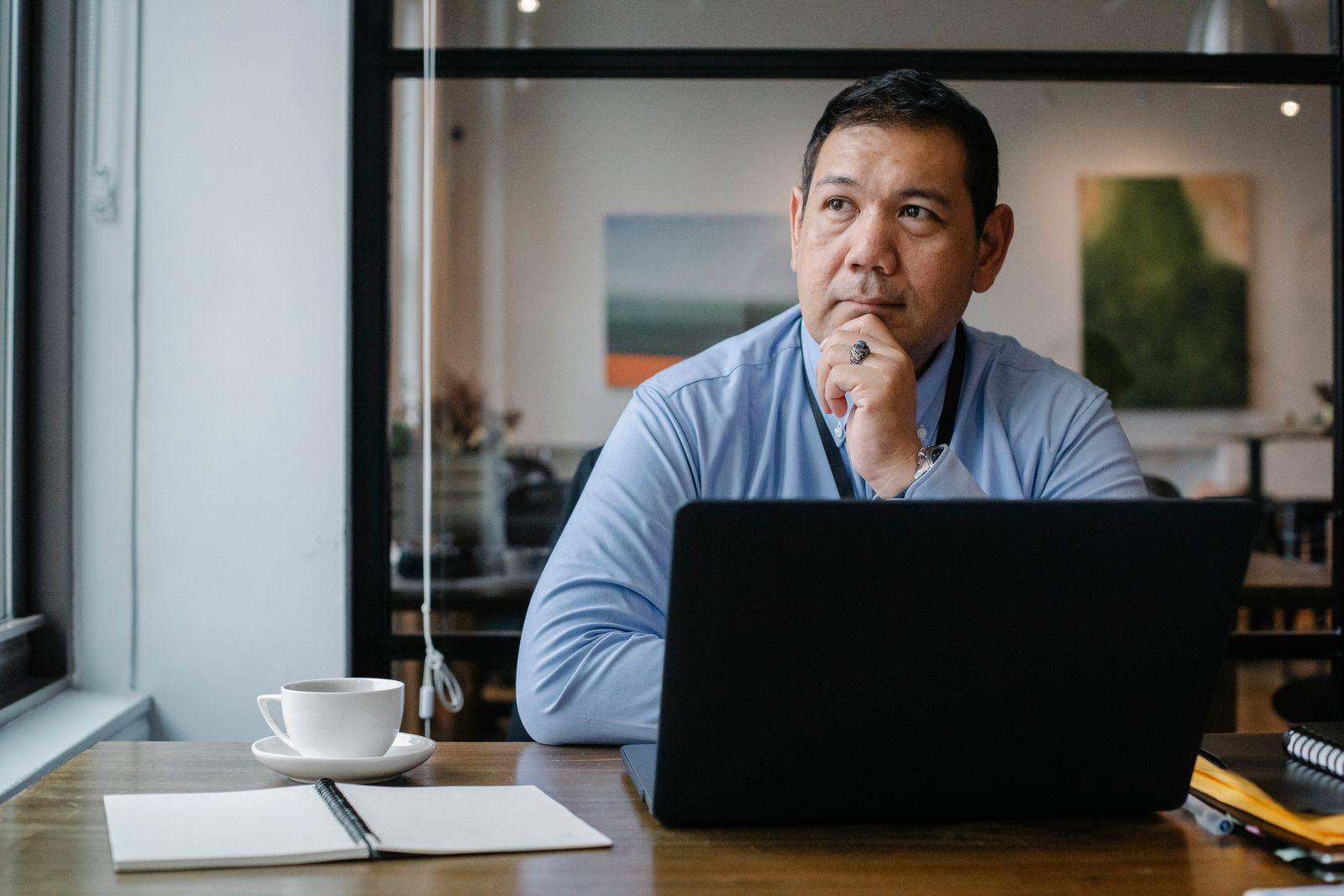 Man at a laptop resting his chin on his hand, thinking