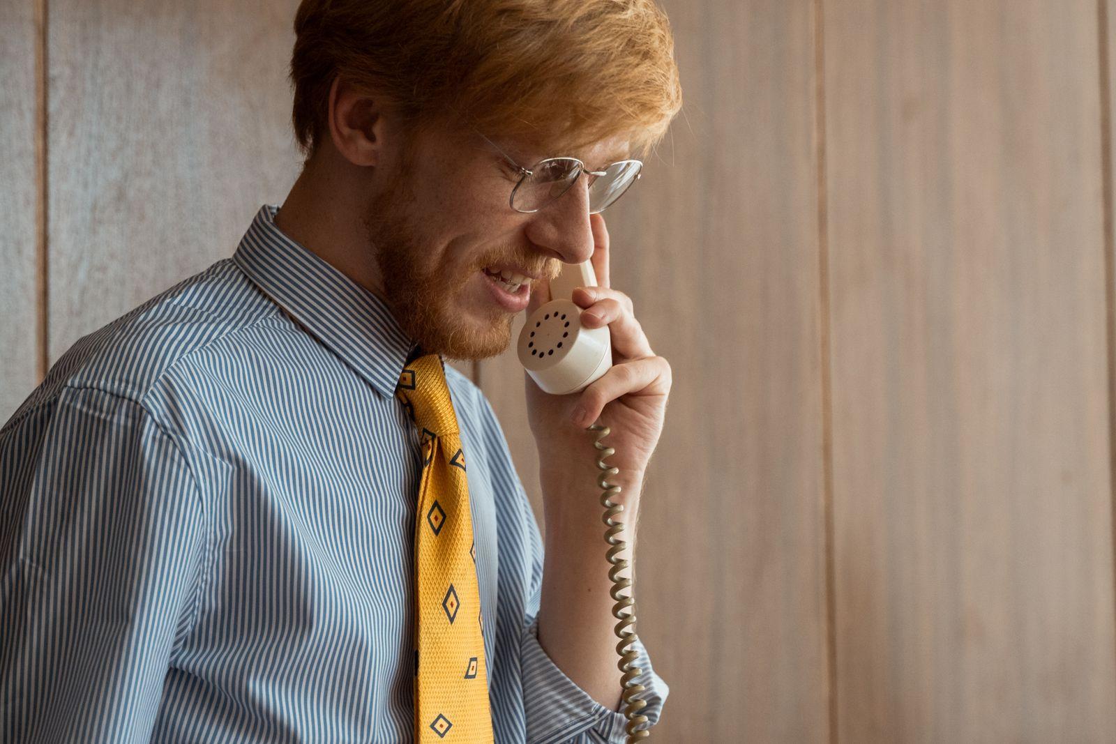 Man in a striped shirt and yellow tie talking on a desk phone