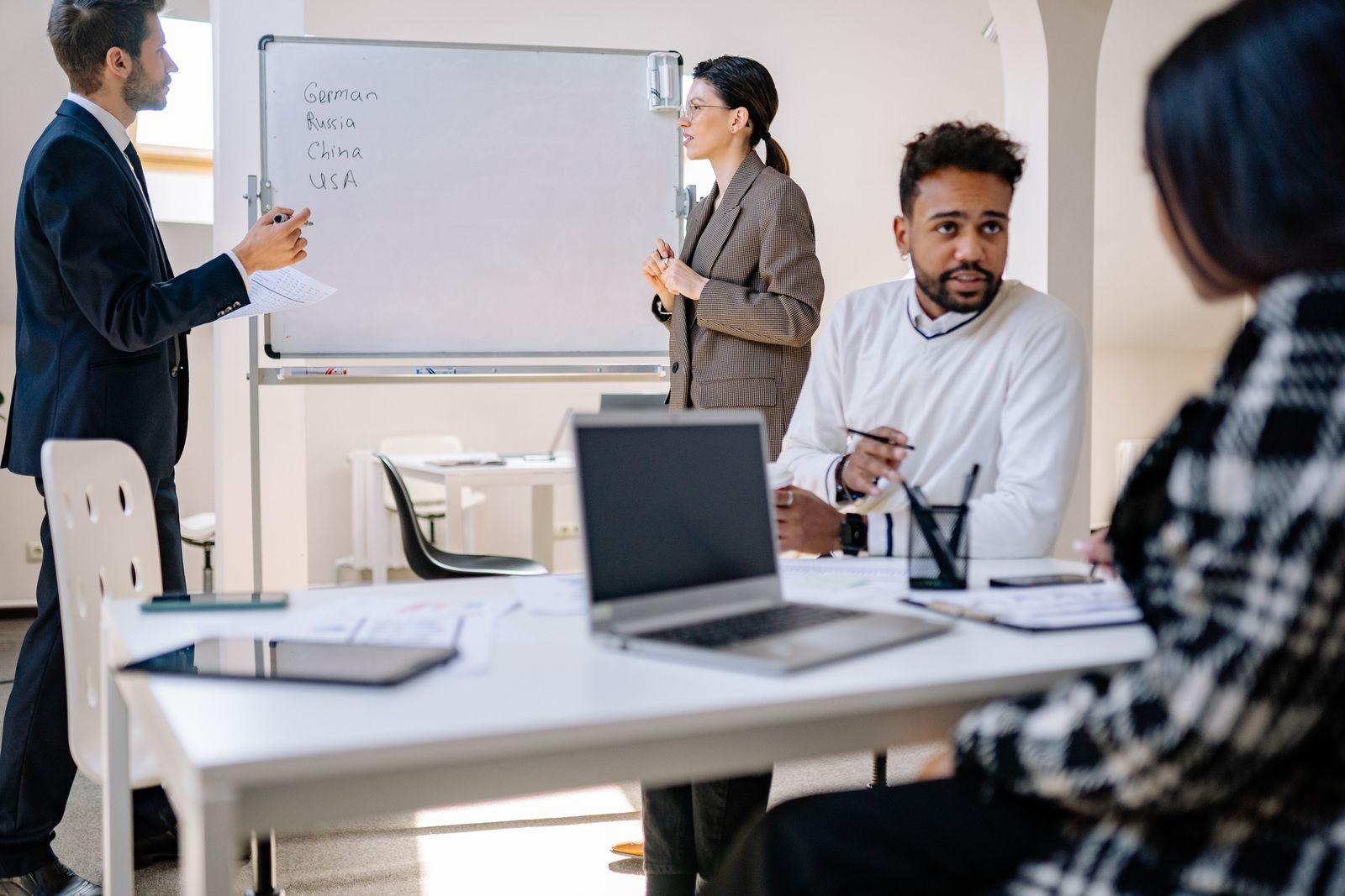 Team meeting with a presenter at a whiteboard and colleagues at laptops